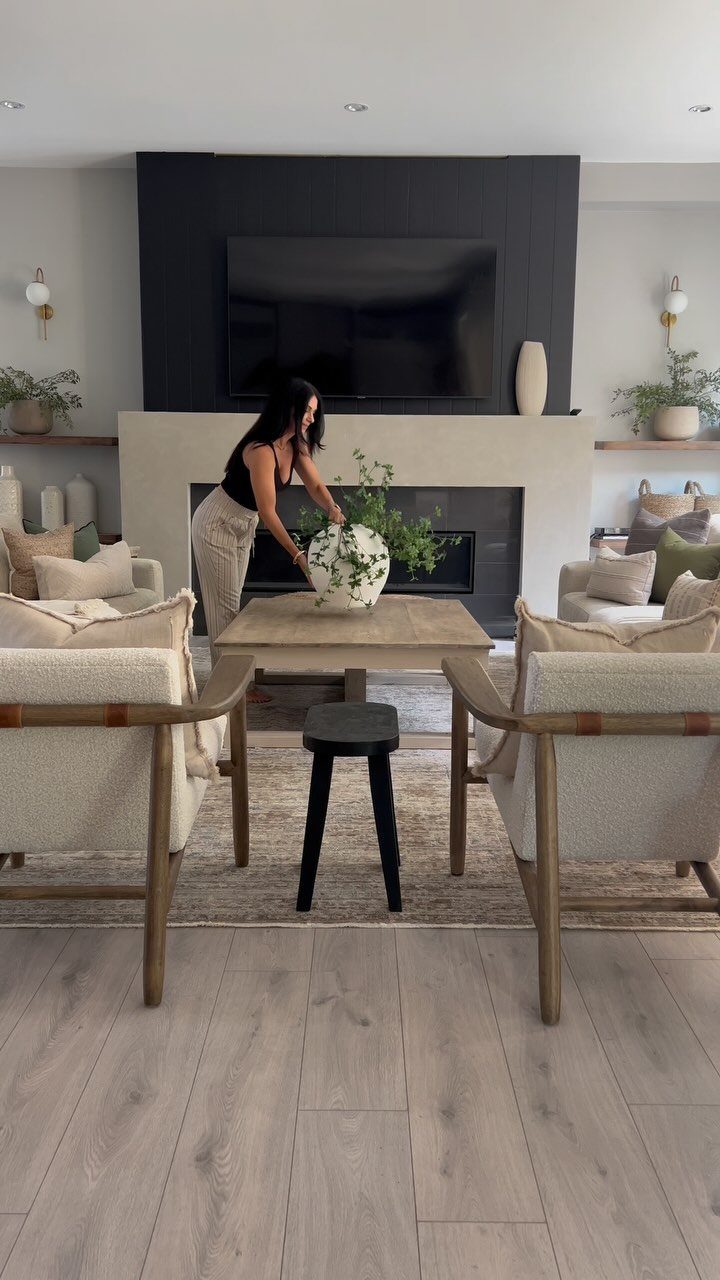 Beige living room with neutral furniture and a woman arranging white flowers.