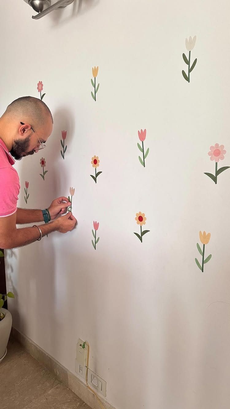 Man applying colorful flower wall decals to a plain white interior wall.