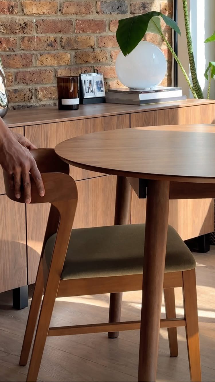 Round wooden dining table and chair set against a rustic red brick wall.