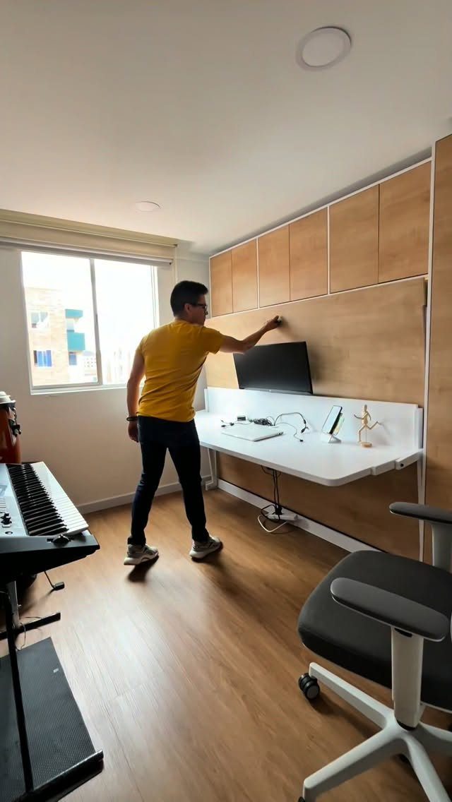 Man standing by a built-in white desk with wooden wall cabinets and monitor.