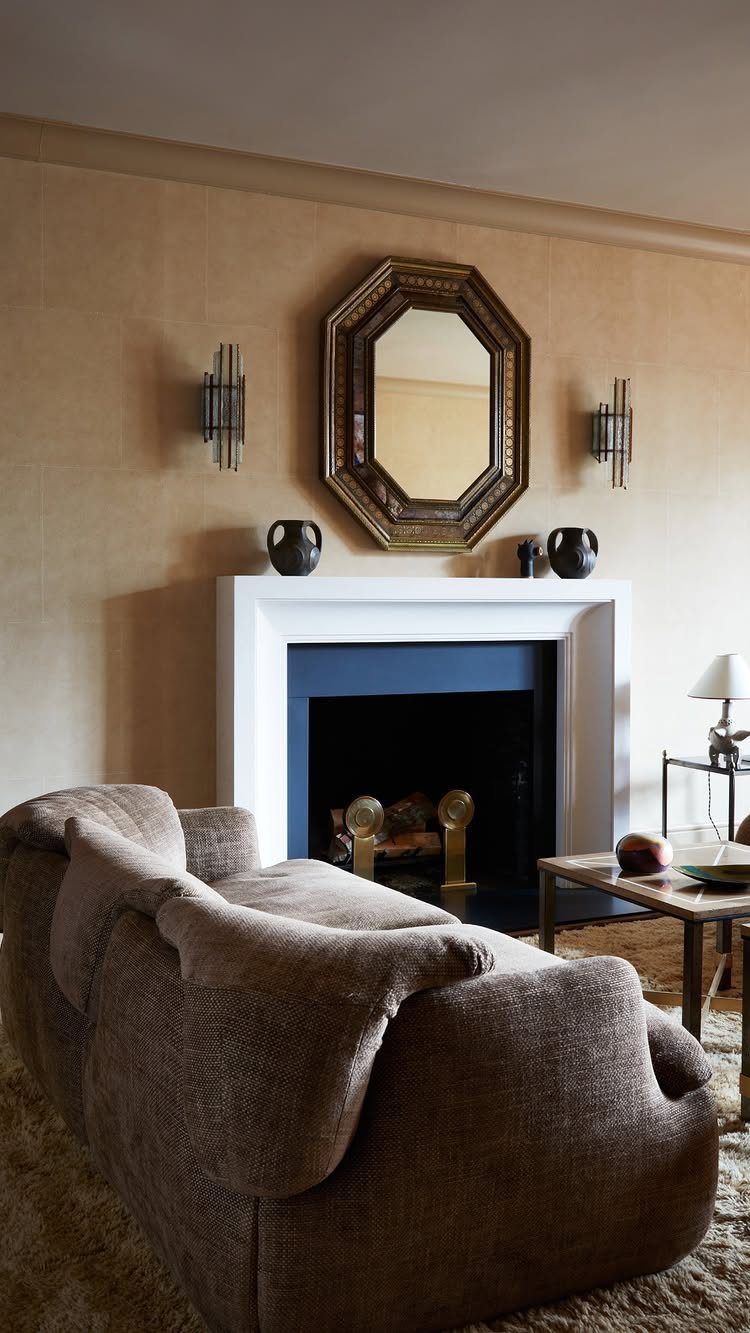 Brown fabric sofa in front of a white fireplace and gold octagonal mirror.