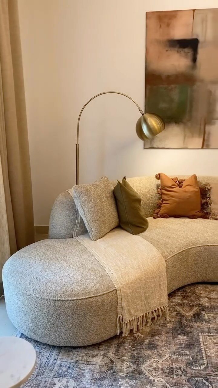 Curved beige sofa with colorful pillows and a gold lamp in a living room