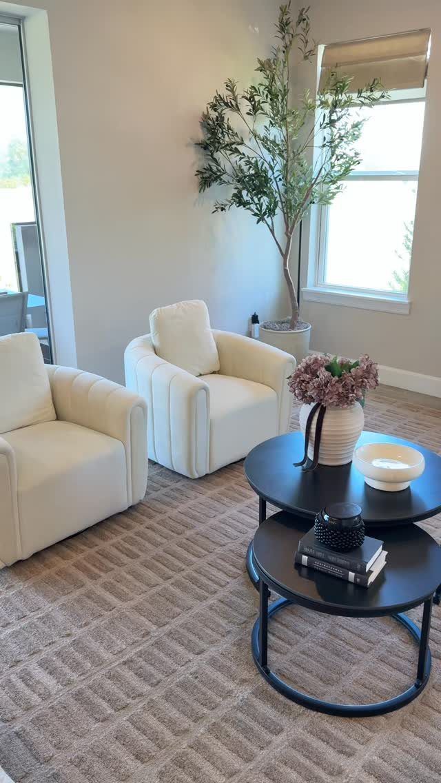 Cream armchairs and black nesting coffee tables on a textured beige area rug.