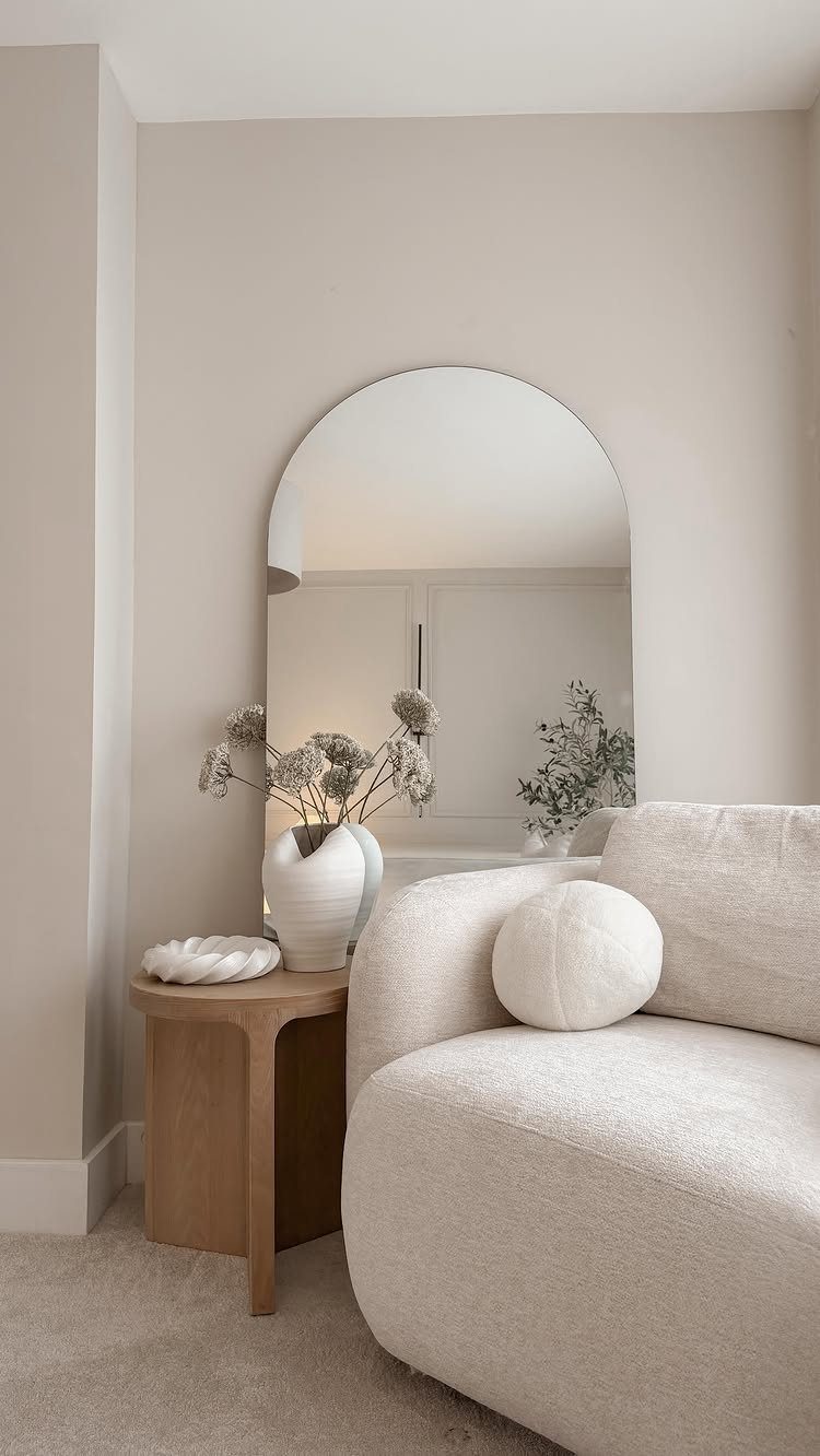 Curved cream sofa and wooden side table next to a large arched wall mirror.