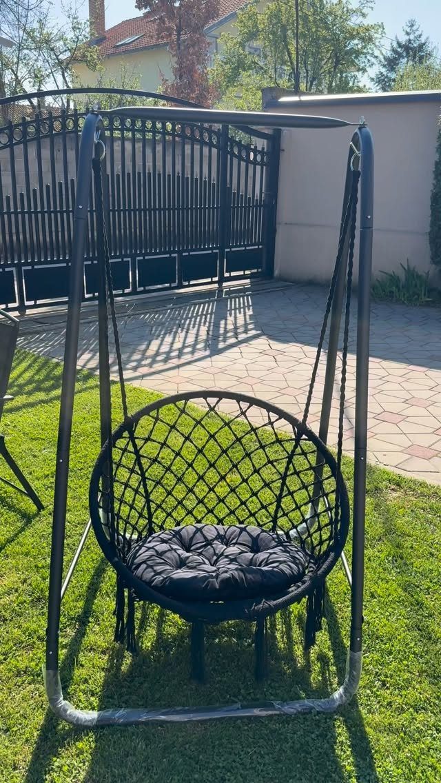 Black hanging egg swing chair with cushion on a sunny green lawn