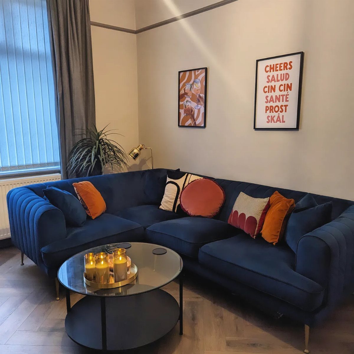 Navy blue velvet sectional sofa with orange pillows and a round black coffee table.