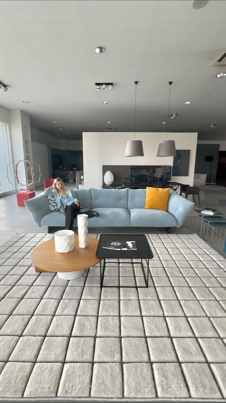 Light blue sofa with a yellow pillow and modern coffee tables on a grey rug