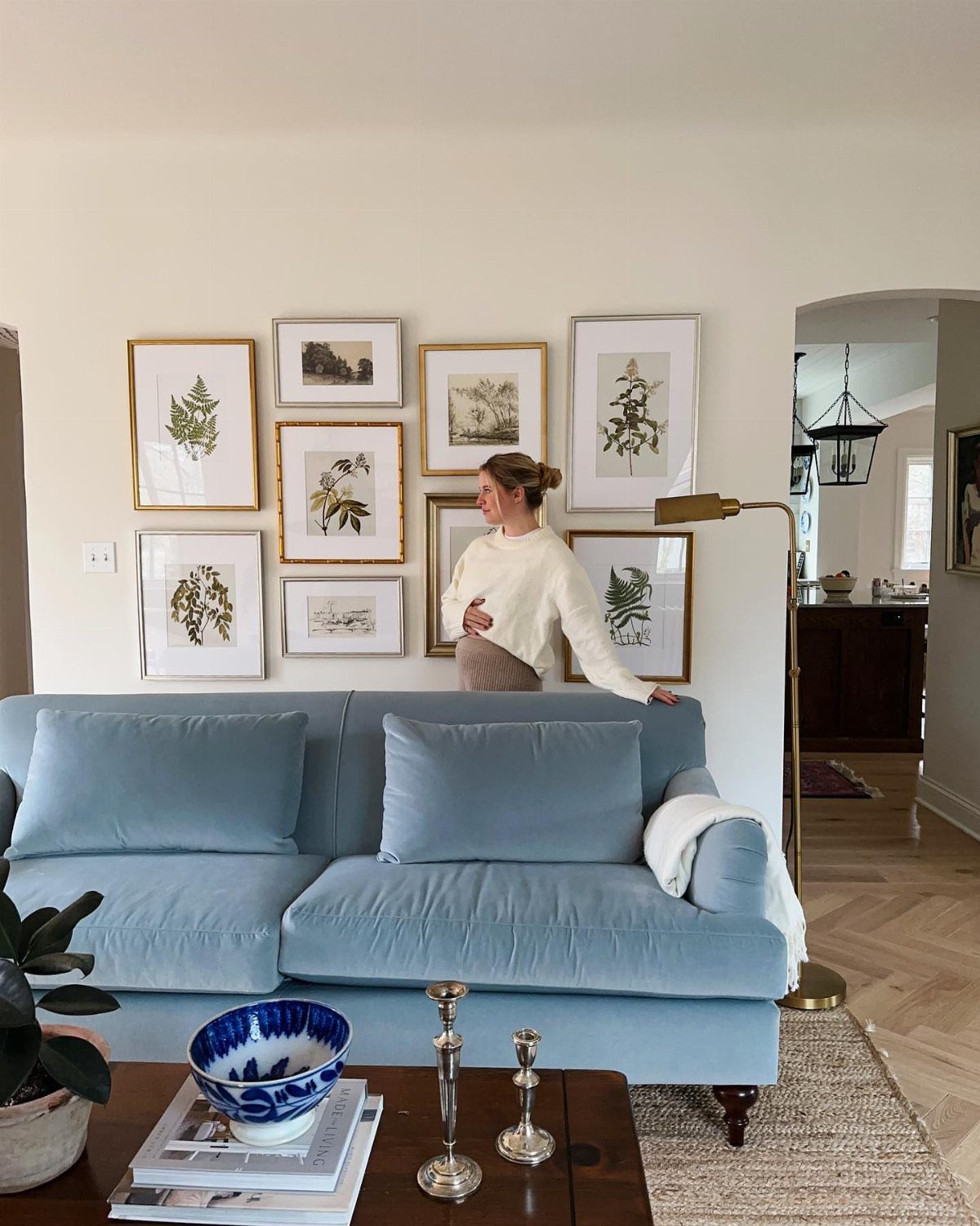 Light blue sofa against warm neutral walls with a botanical gallery wall above.