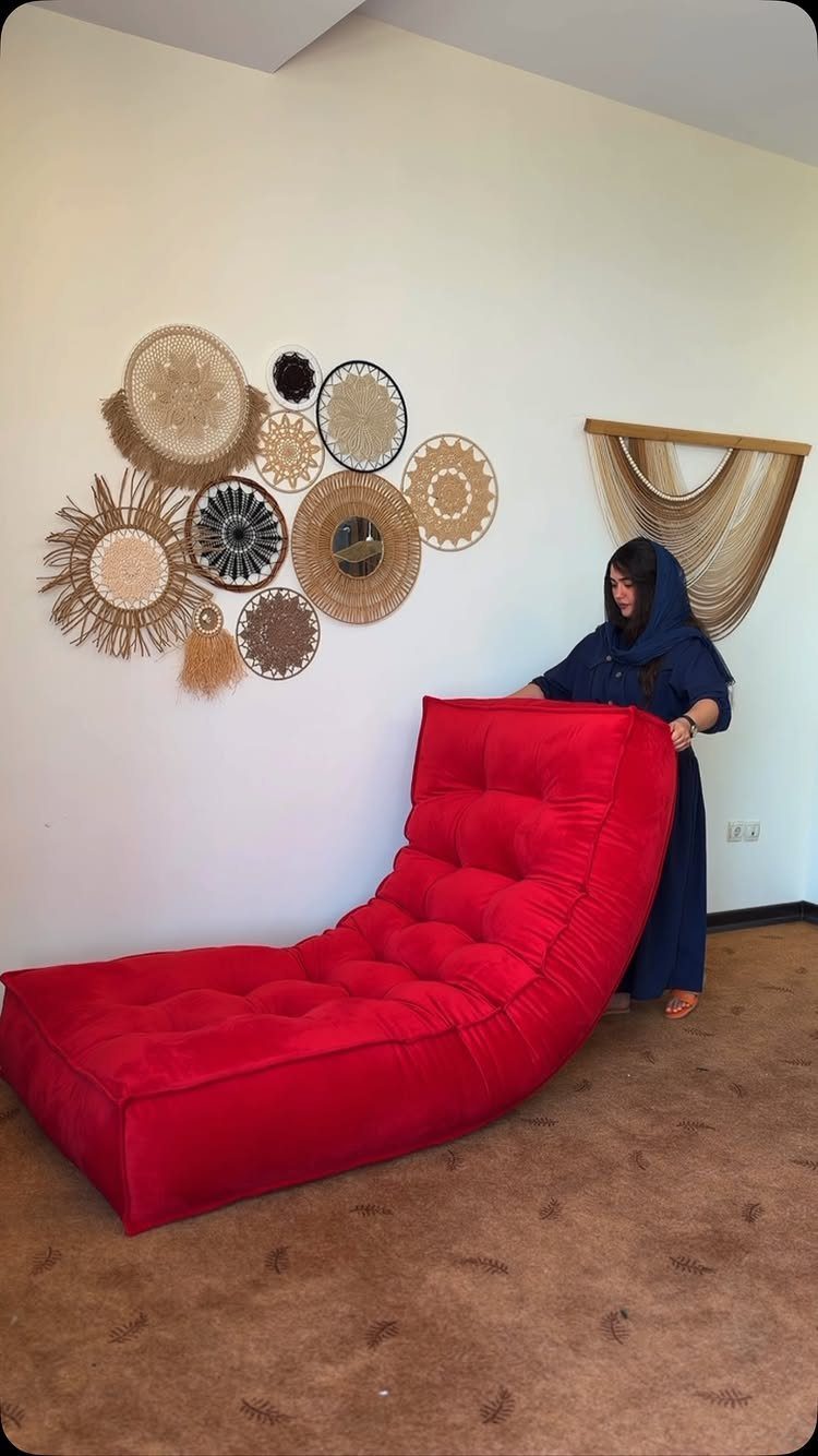 Red tufted lounge chair with woven wall decorations and a woman in blue.