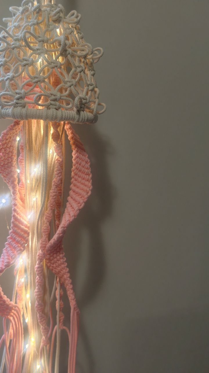 Boho light fixture with white macramé shade and pink tassels glowing with fairy lights.