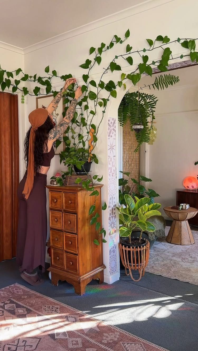 Woman tending to climbing indoor plants next to a wooden dresser and patterned rug.