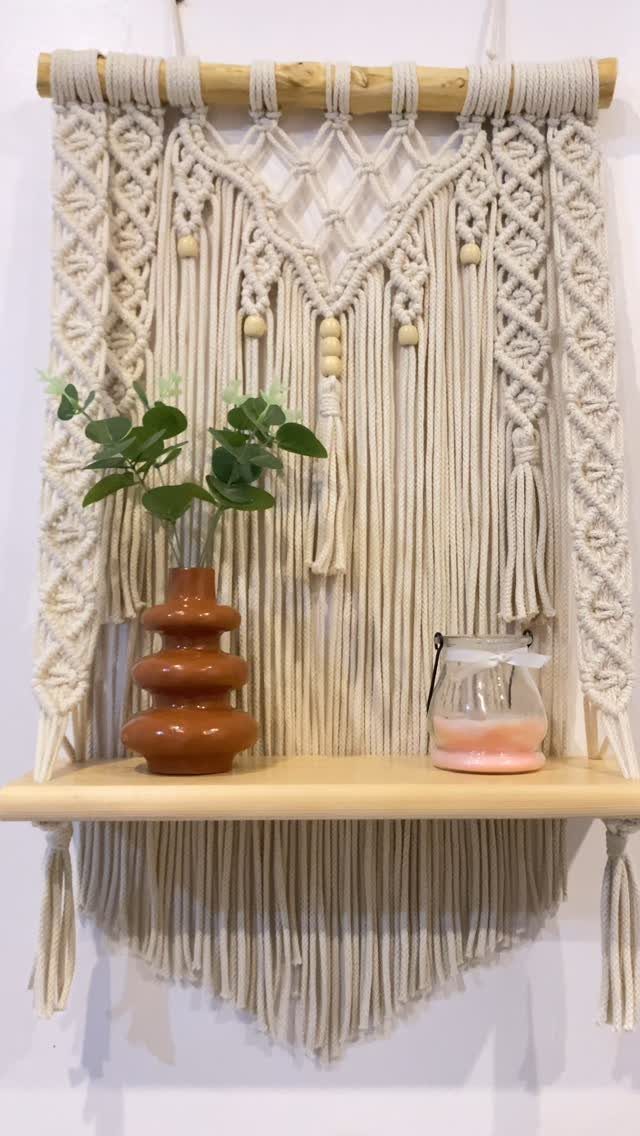 Macramé wall hanging with a wooden shelf holding a vase and glass jar.