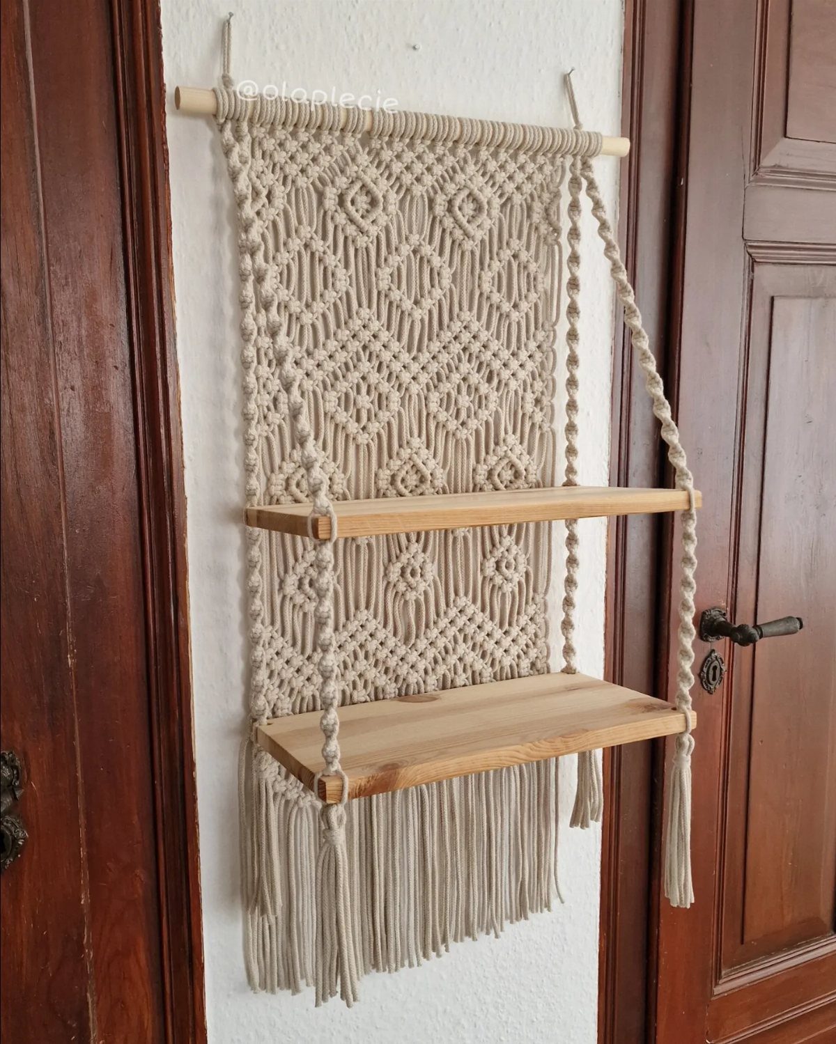 Macramé wall hanging with two integrated wooden shelves suspended from a wooden dowel.