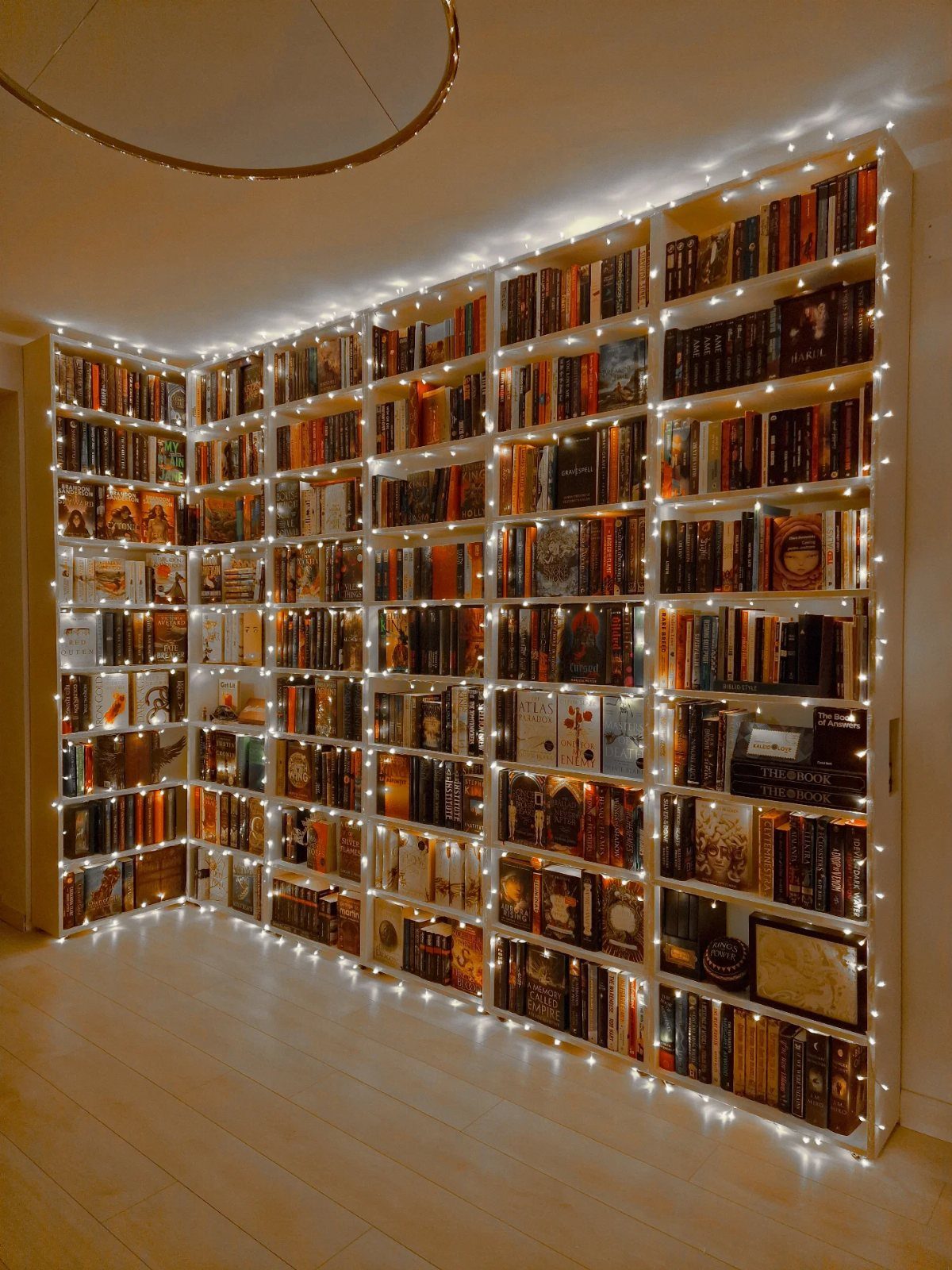 White bookshelf filled with books and decorated with glowing warm white fairy lights.