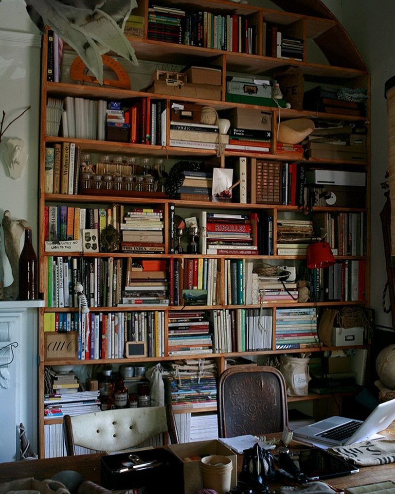 Wooden bookshelf densely packed with books, boxes, and collectibles in a home office.