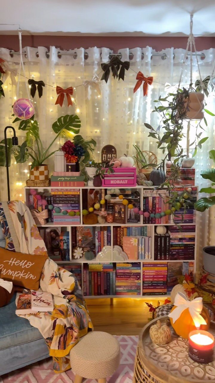 White bookshelf with color sorted books, indoor plants, and festive room decorations.