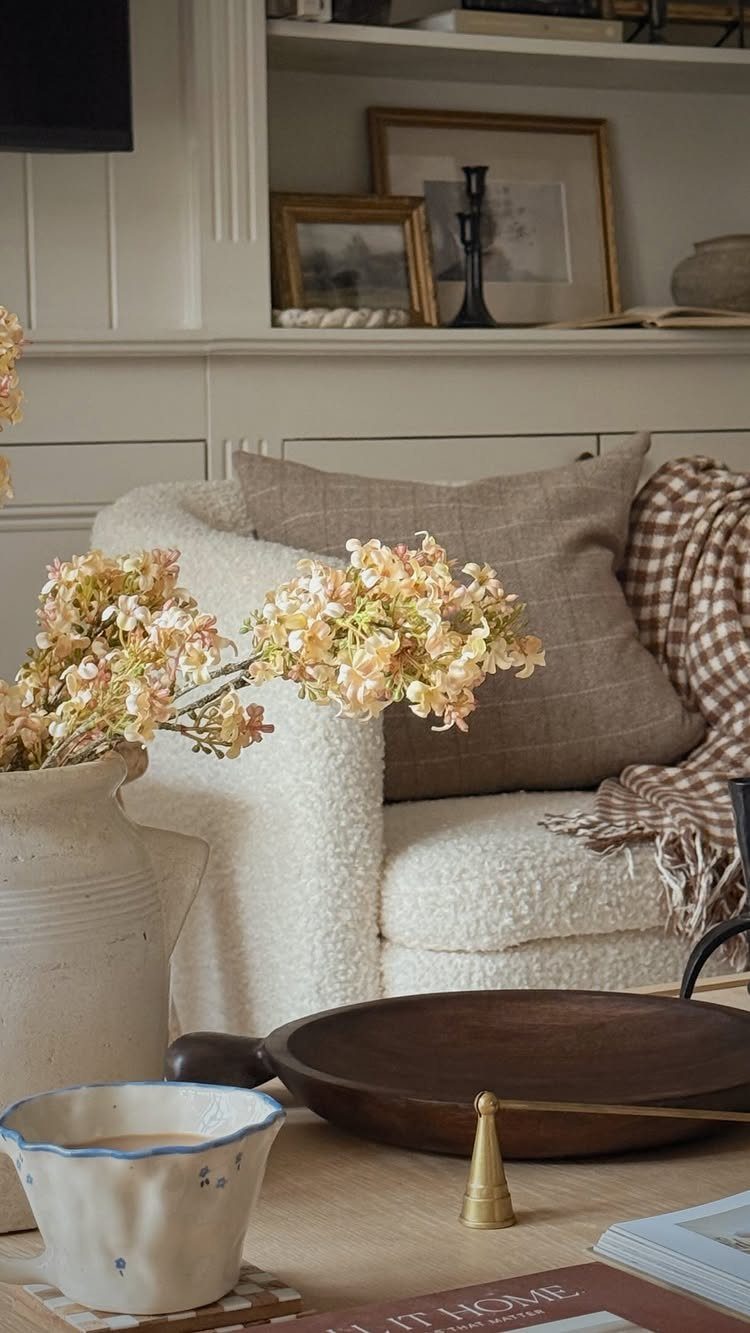 White bouclé armchair with brown pillow and framed art on a bookshelf background.