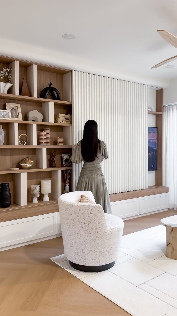 Sliding white slatted panel hiding a TV within a large wooden bookshelf unit.
