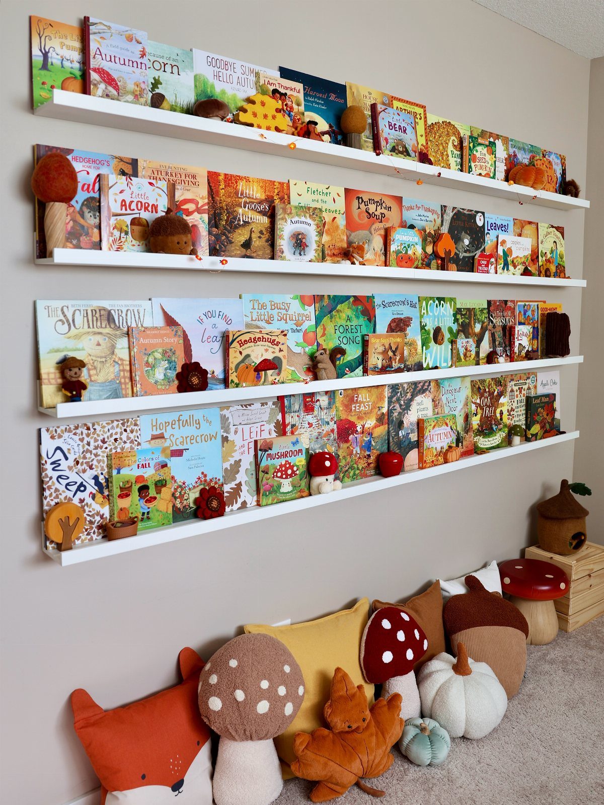 White floating shelves with children's books and autumn-themed decor and plush pillows.