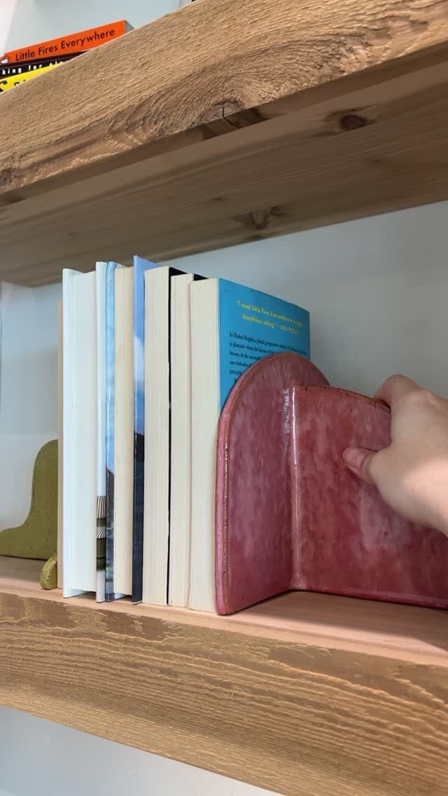 Red curved bookend holding a row of books on a wooden shelf.