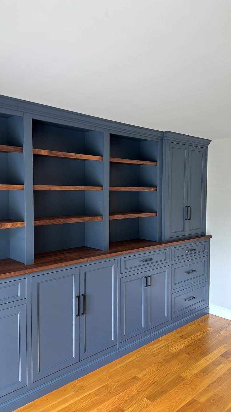 Navy blue built-in bookshelves with base cabinets and dark wood shelving on light floors.