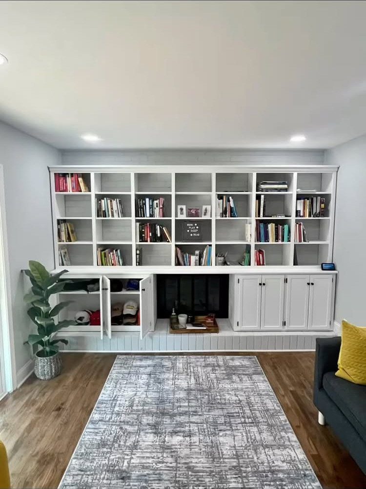 White built-in bookshelves and cabinets surrounding a black fireplace in a living room.