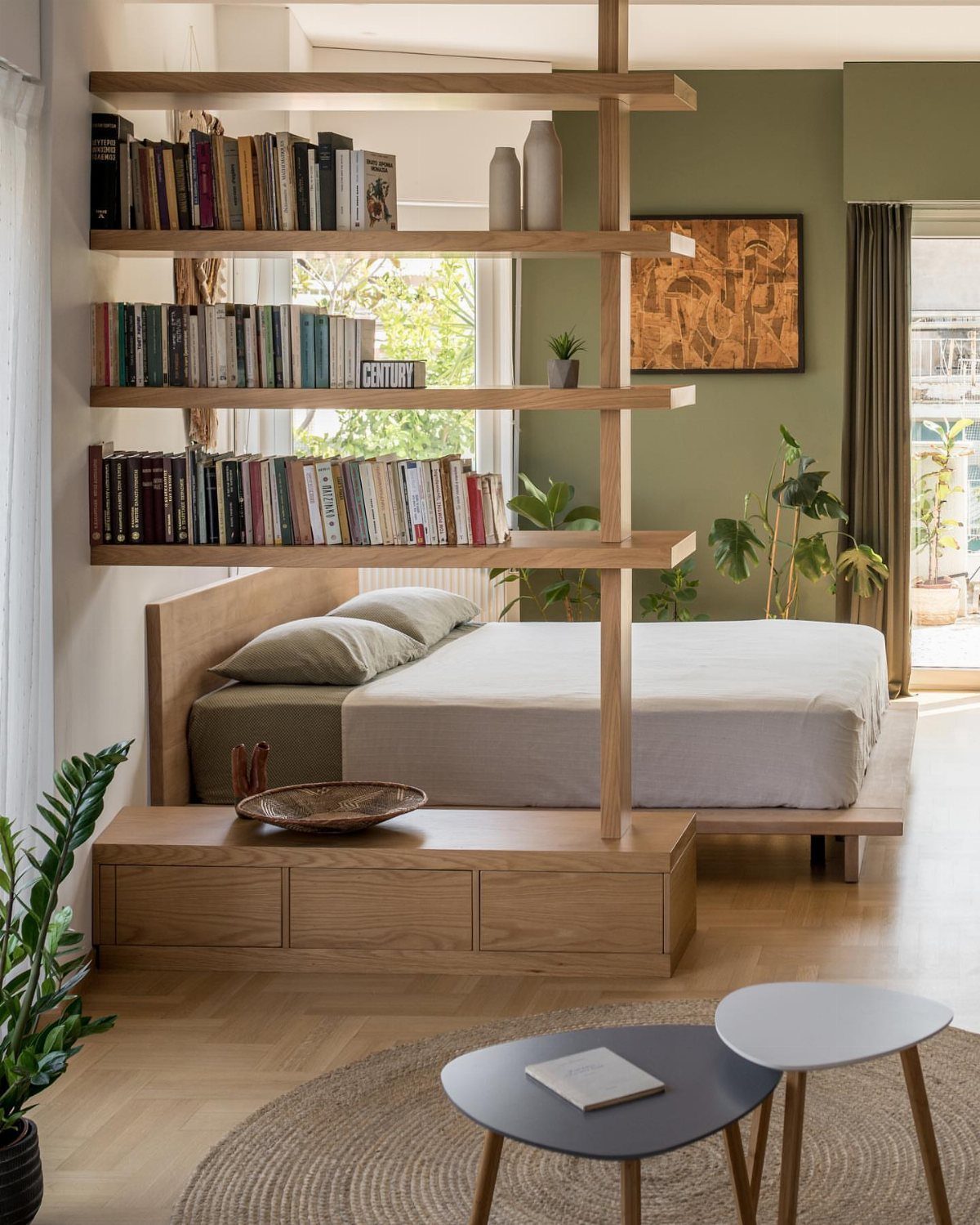 Wooden open bookshelf acting as a room divider between a bed and living area.