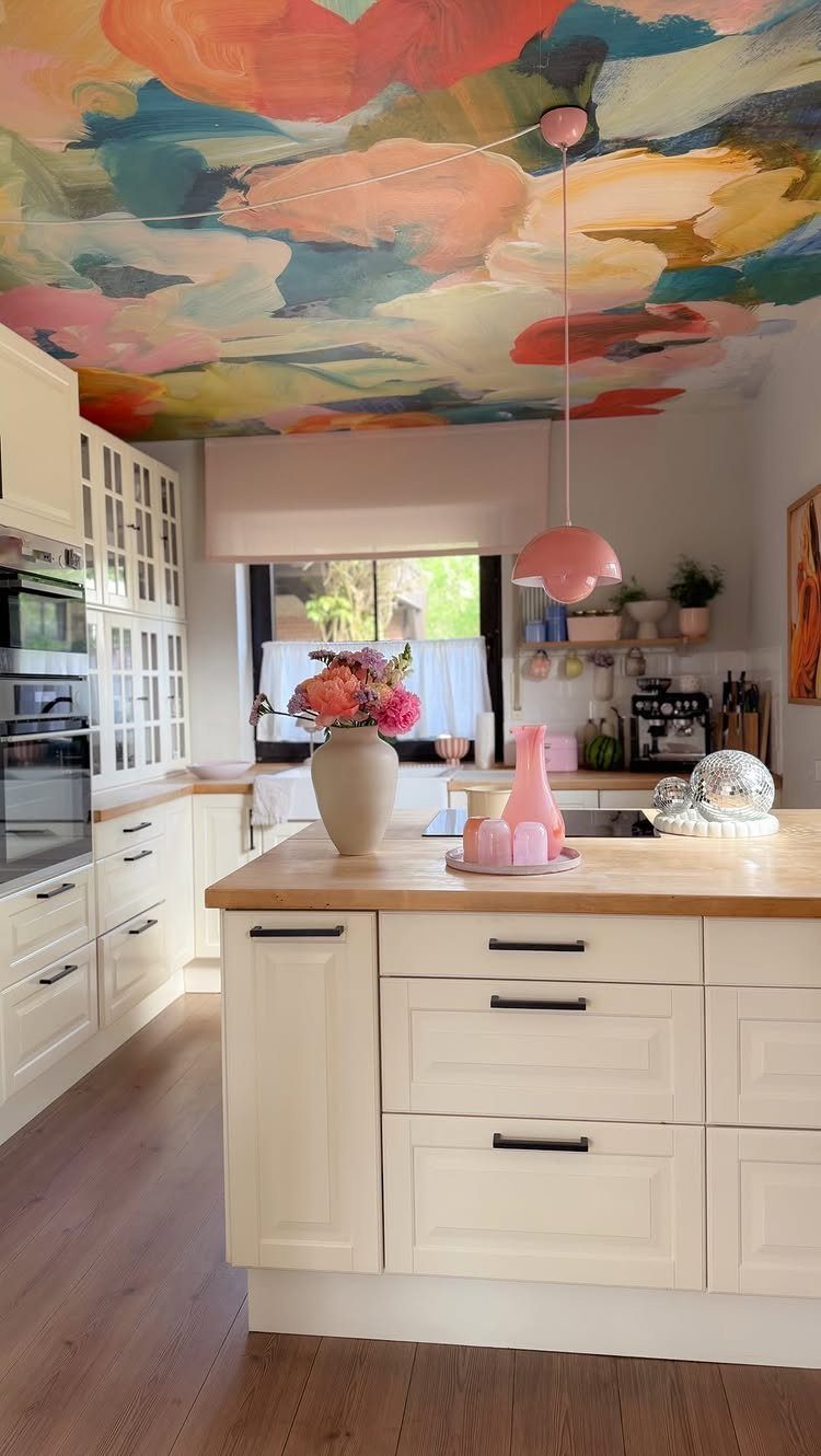 Colorful abstract mural on a kitchen ceiling above white cabinets and wooden island.