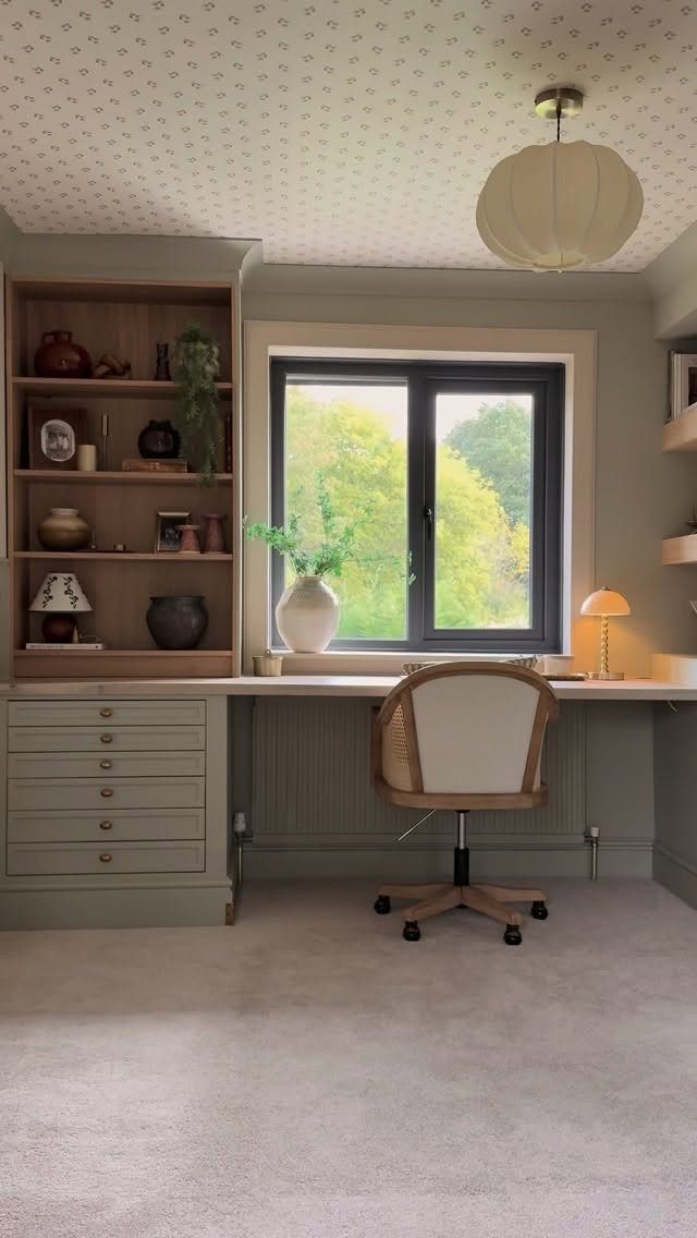 Home office with patterned ceiling wallpaper, built-in desk, and white pleated pendant lamp.