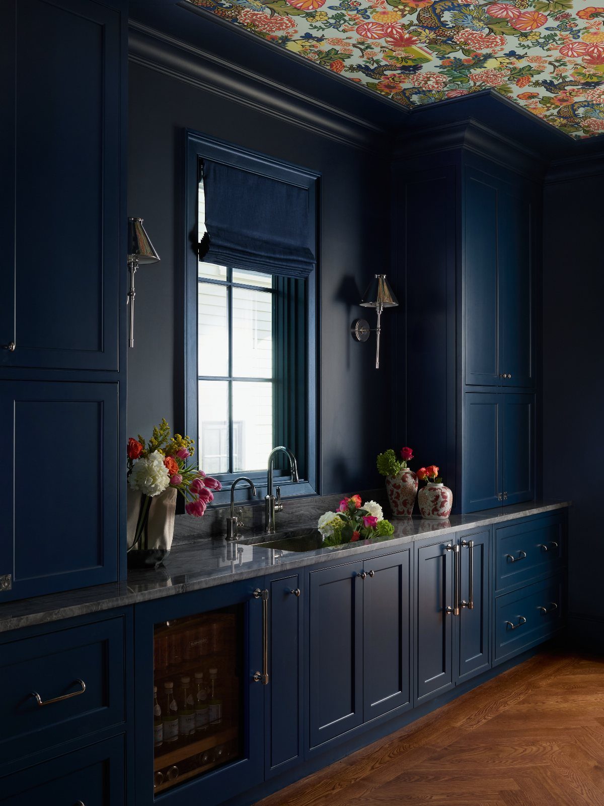 Deep blue kitchen cabinets and walls with colorful floral wallpaper on the ceiling.