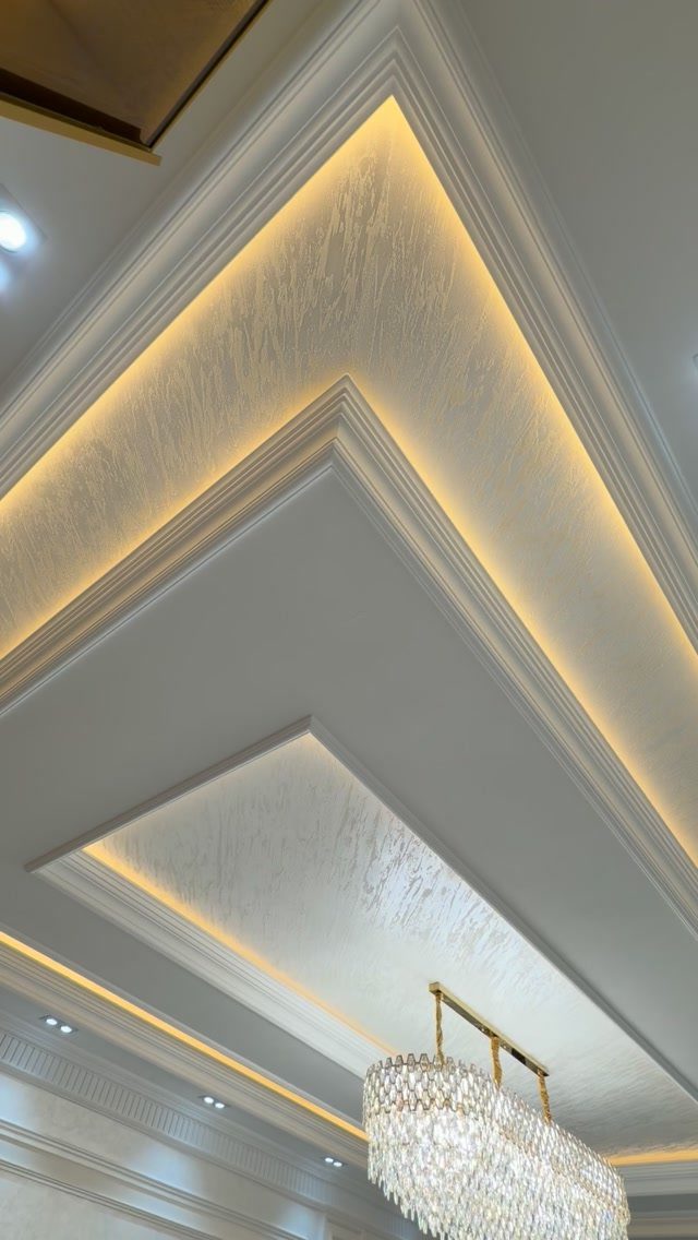 Tray ceiling with textured white wallpaper, warm cove lighting, and a crystal chandelier.