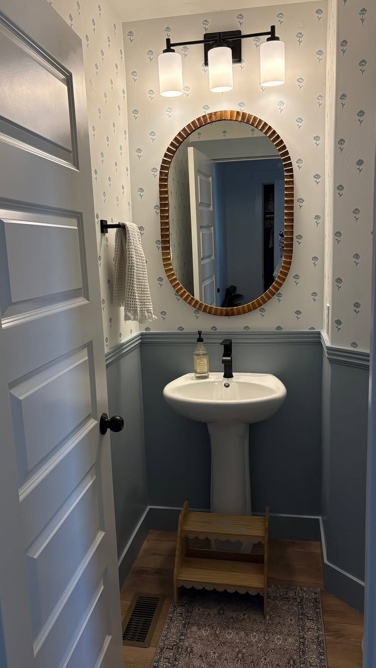 Small bathroom with blue lower walls, white chair rail, and patterned wallpaper.
