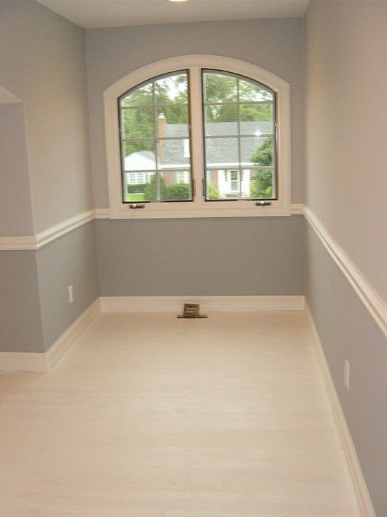 White chair rail installed on light grey walls in a room with arched window.
