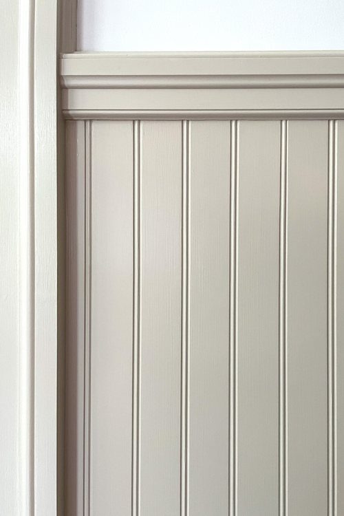 Layered chair rail molding atop light beige vertical beadboard wall paneling.