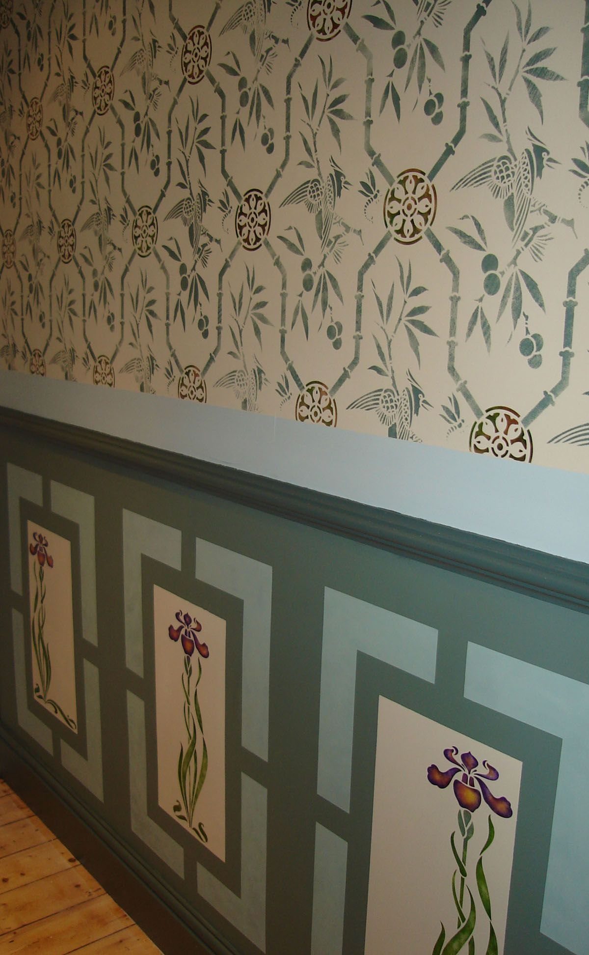 Stenciled floral iris designs on a teal wall below a horizontal chair rail.