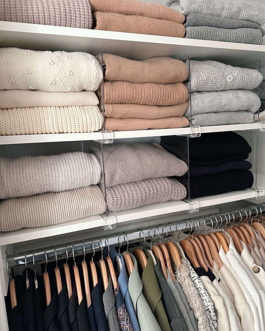 White closet shelves with acrylic dividers organizing folded neutral-colored sweaters and hanging clothes.