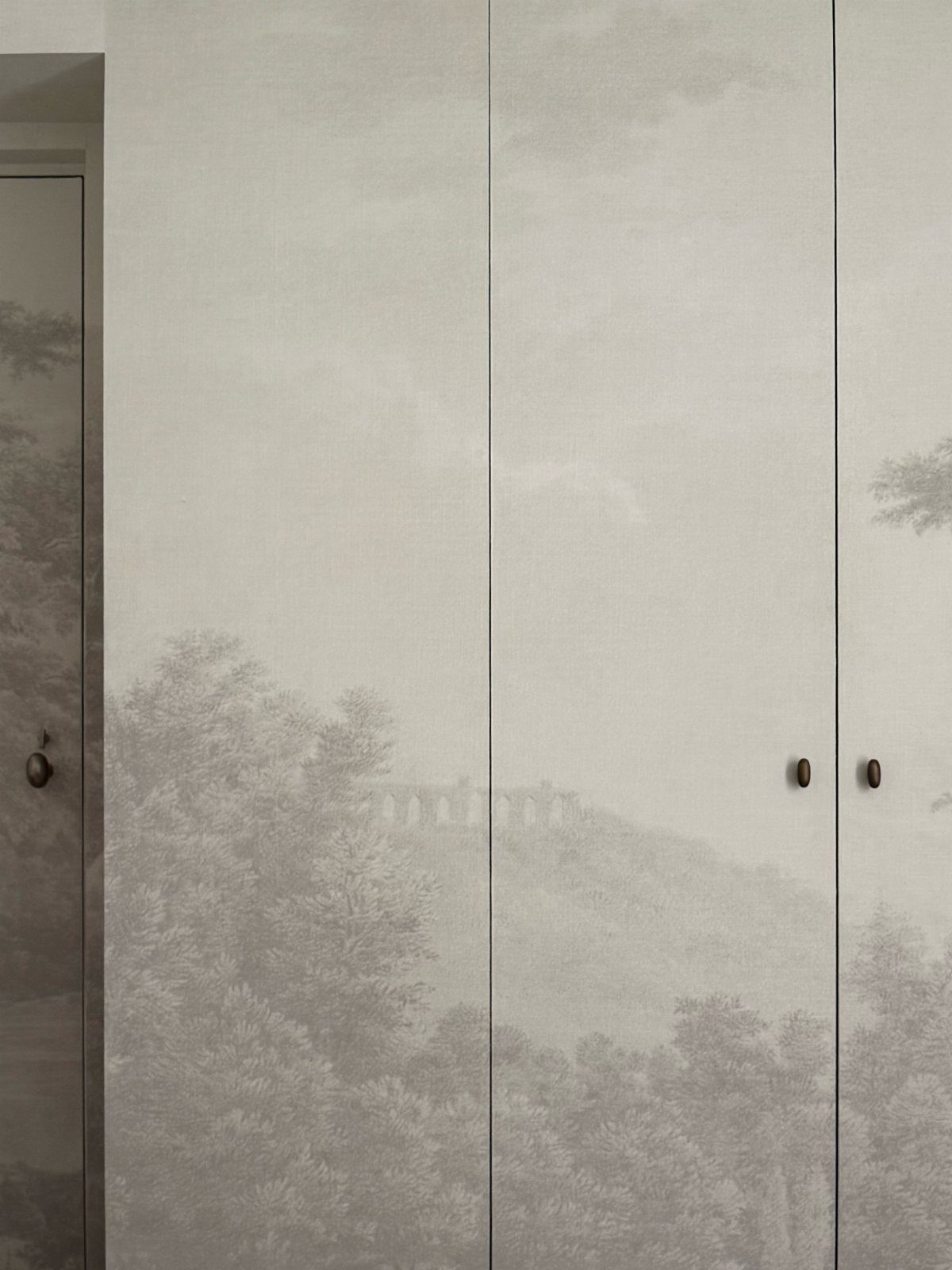 Closet doors featuring a grey landscape wallpaper with small dark circular door knobs.