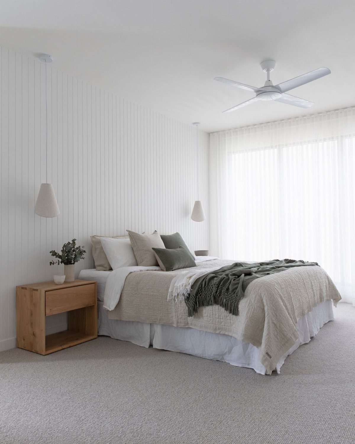 White ceiling fan in a bright coastal bedroom with white paneled walls.