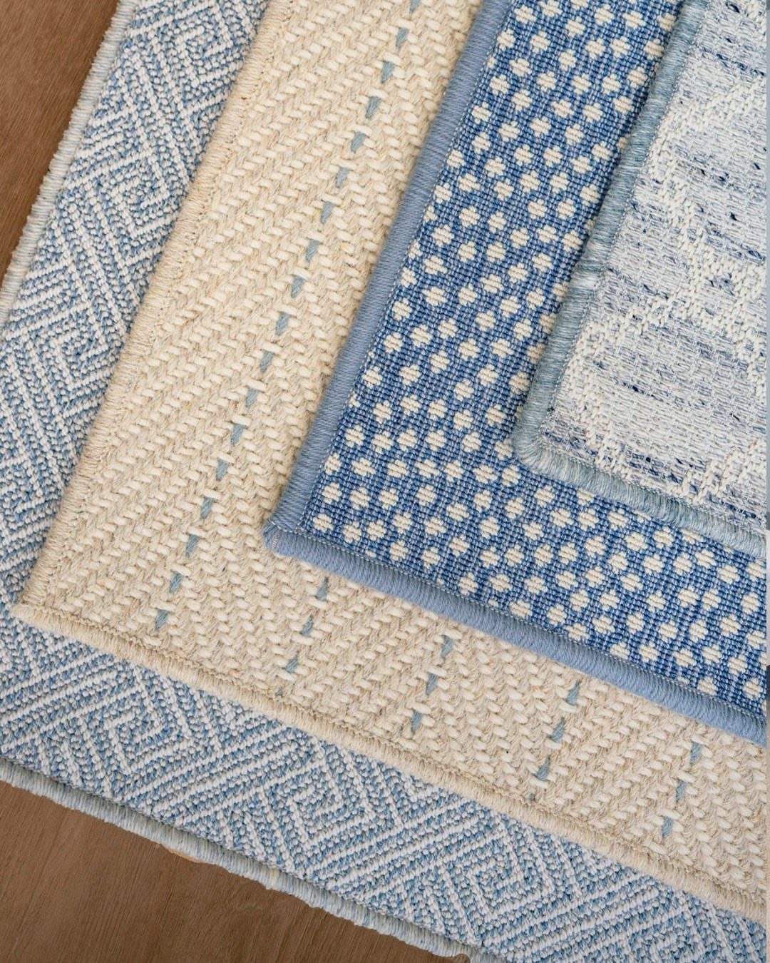 Three layered area rugs in blue and cream tones on a wooden floor.