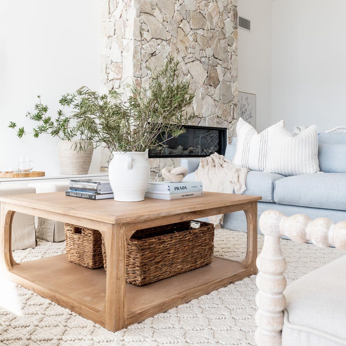 Wooden coffee table with woven baskets and a white vase in a coastal living room