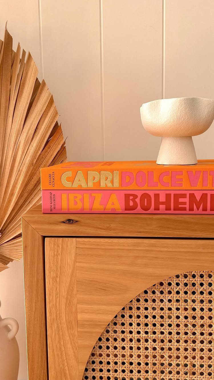 Stacked orange and pink books with a white bowl on a wooden cabinet.