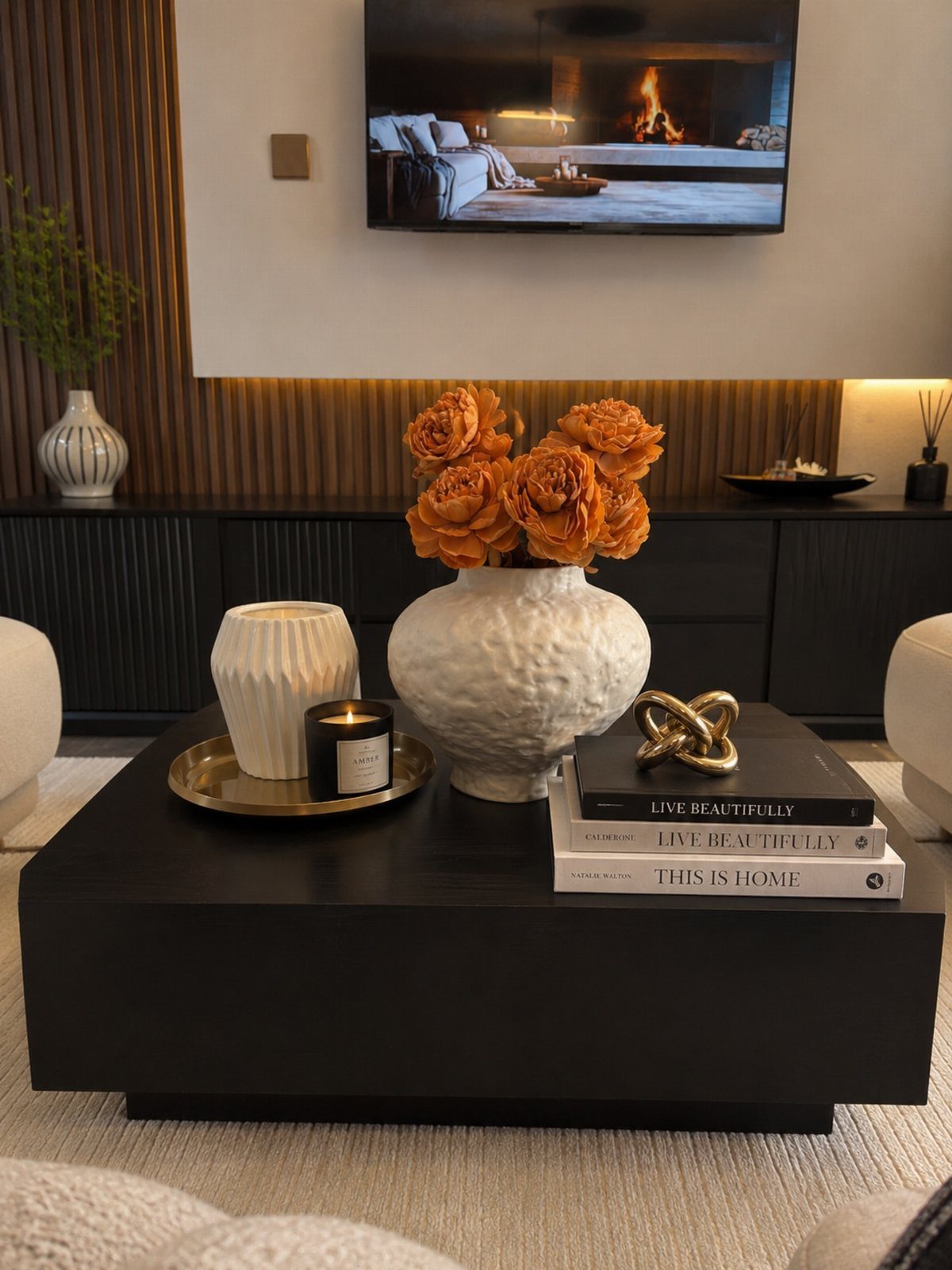 Black coffee table decorated with orange roses in a white vase and stacked books.