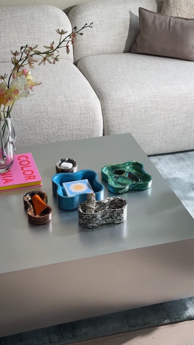 Grey coffee table with colorful decorative bowls, a pink book, and floral vase.