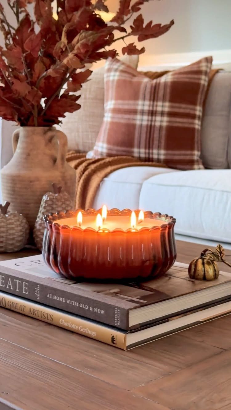 Autumnal coffee table decor with a lit amber candle, books, and fall leaves.