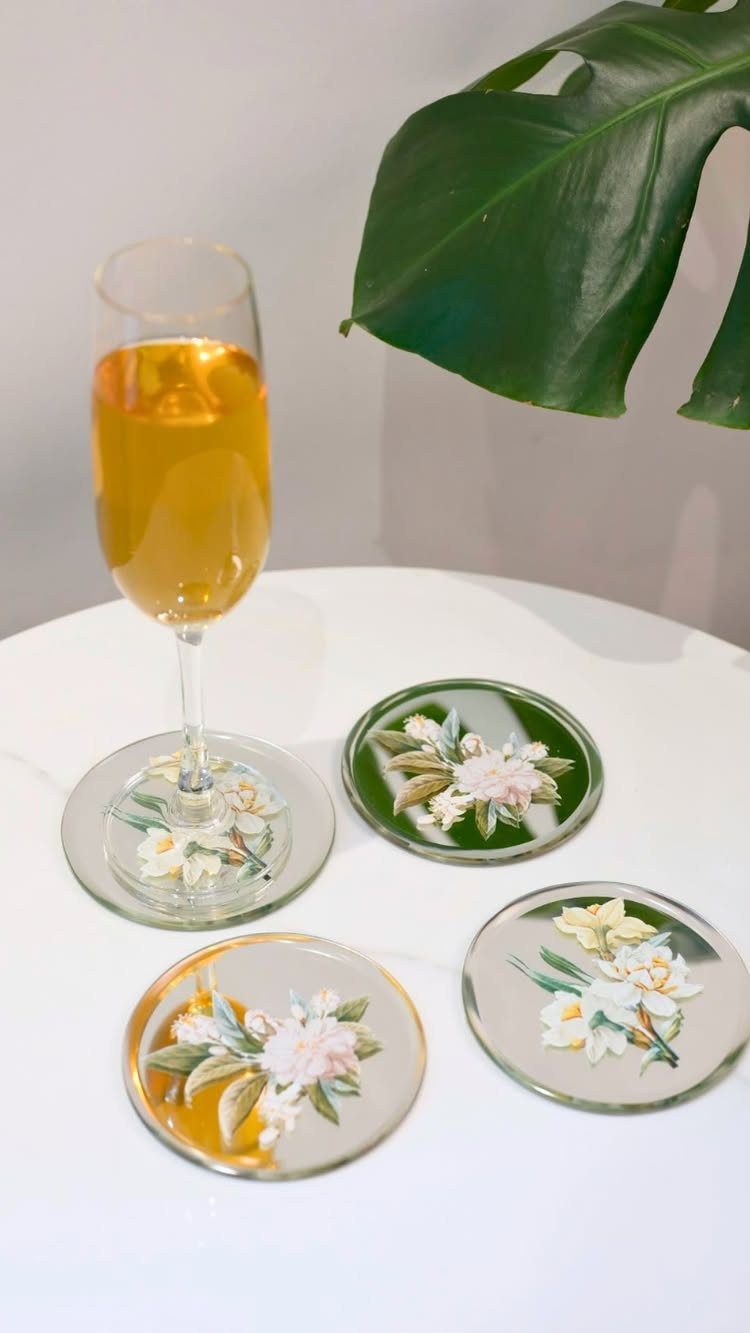 Glass coasters with floral designs on a white table with a champagne flute.