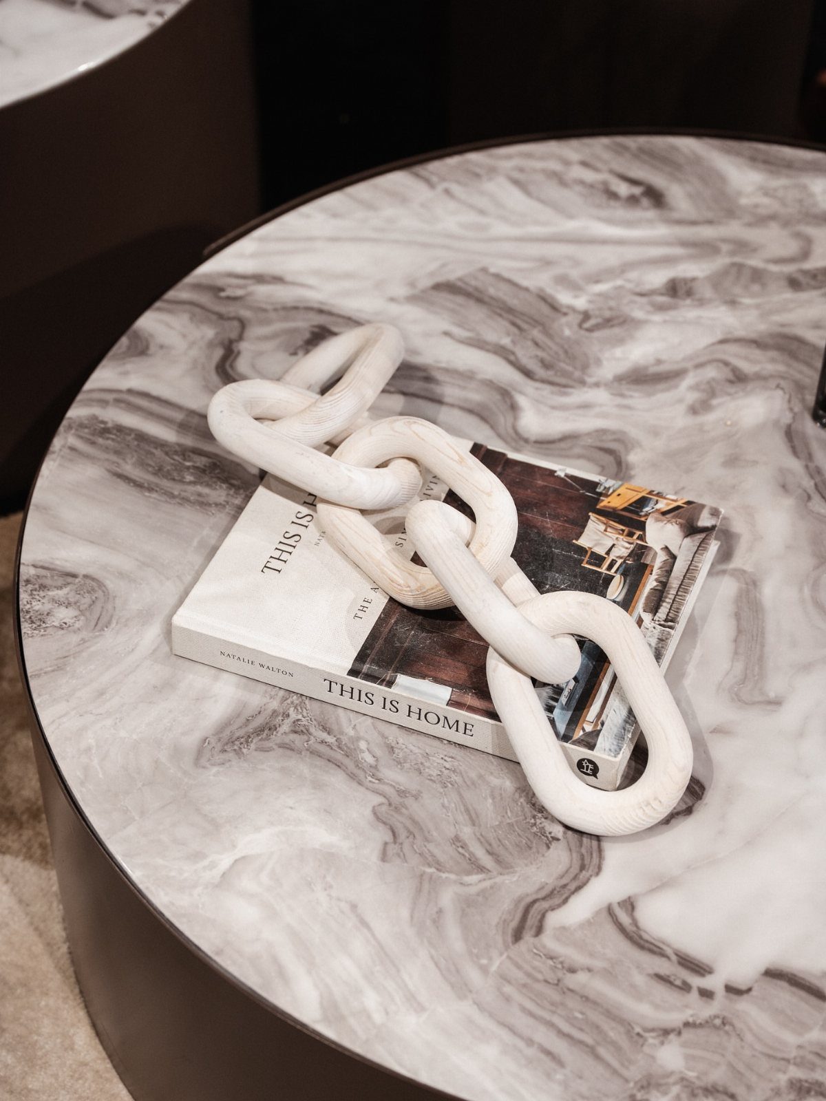 White decorative chain link sculpture resting on a book atop a marble coffee table.