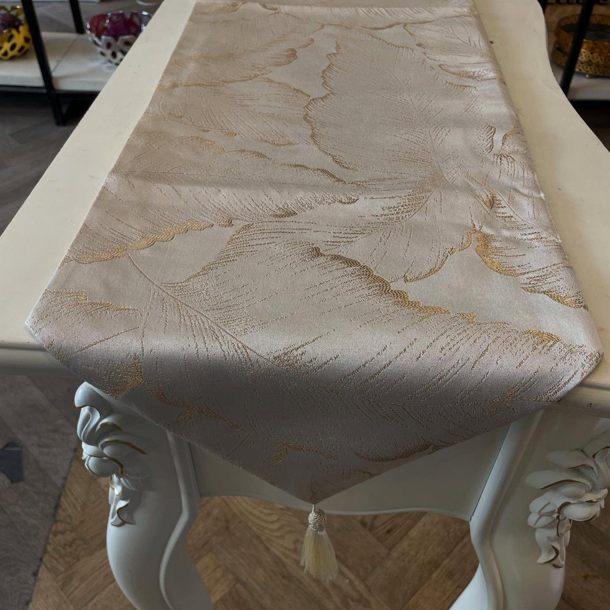 Champagne fabric table runner with gold leaf patterns on a white ornate table.