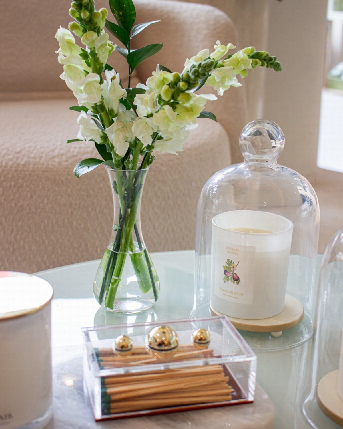 White flowers in a vase and a candle under a glass cloche on a table.