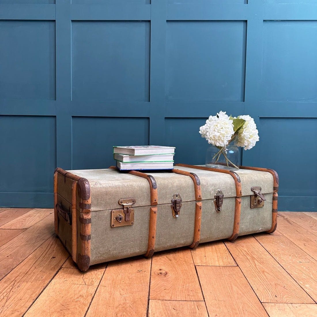 Vintage steamer trunk coffee table with books and white flowers on a wooden floor.