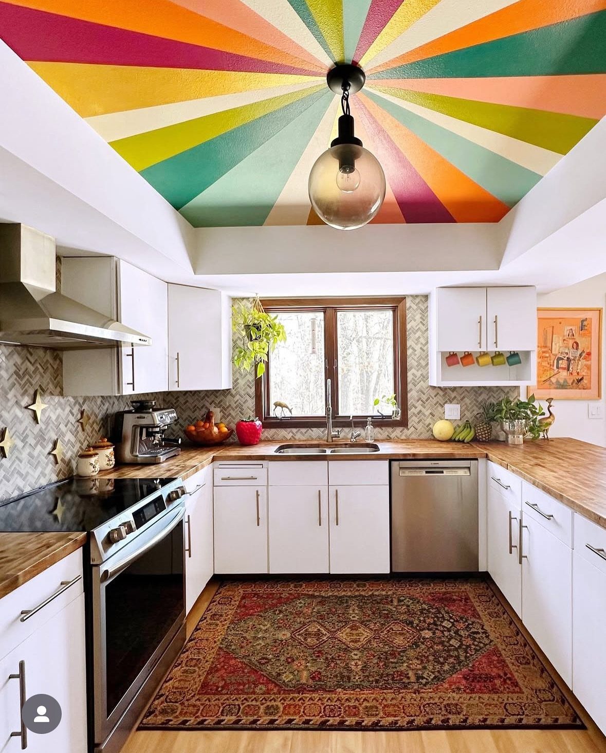Colorful sunburst painted ceiling in a white kitchen with a patterned red rug.